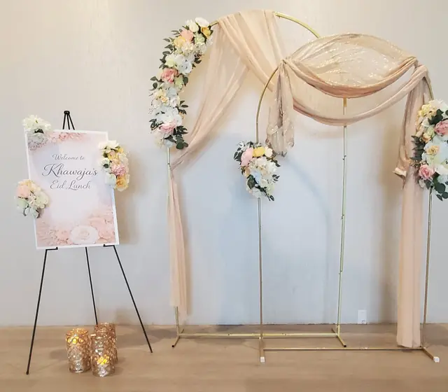 Two gold hoop arches with peach chiffon draping and pastel florals beside a floral welcome sign